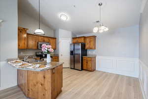 Kitchen with appliances with stainless steel finishes, sink, hanging light fixtures, kitchen peninsula, and light wood-type flooring