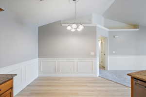 Unfurnished dining area featuring vaulted ceiling, a notable chandelier, and light hardwood / wood-style flooring