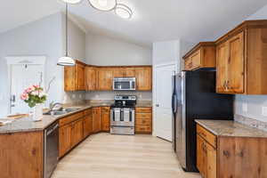 Kitchen featuring decorative light fixtures, lofted ceiling, sink, light stone countertops, and appliances with stainless steel finishes