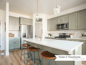 Kitchen featuring sink, light wood-type flooring, pendant lighting, stainless steel appliances, and a center island with sink