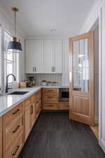 Kitchen featuring sink, white cabinetry, stainless steel microwave, and crown molding