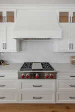 Kitchen with stainless steel gas stovetop, backsplash, custom exhaust hood, and white cabinets