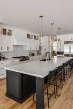 Kitchen featuring custom exhaust hood, a spacious island, hanging light fixtures, sink, and a breakfast bar area