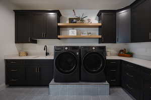 Laundry area featuring sink, cabinets, tile patterned floors, and washing machine and clothes dryer