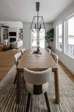 Dining area with wood-type flooring, built in features, ceiling fan with notable chandelier, and crown molding