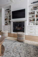 Living room with a fireplace, light hardwood / wood-style floors, built in shelves, and crown molding