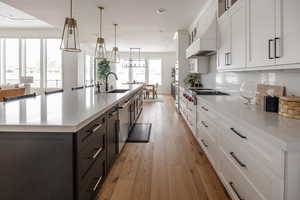 Kitchen featuring a large island with sink, white cabinets, hanging light fixtures, and custom range hood