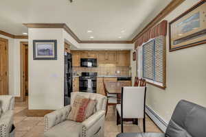 Kitchen with black appliances, crown molding, baseboard heating, and decorative backsplash