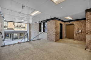 Interior space with brick wall, carpet flooring, a paneled ceiling, and a healthy amount of sunlight