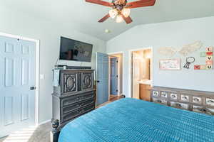 Carpeted bedroom featuring ensuite bath, vaulted ceiling, and ceiling fan