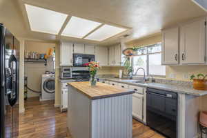 Kitchen with sink, white cabinetry, butcher block countertops, a center island, and black appliances