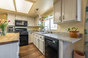 Kitchen with sink, black appliances, white cabinets, and light stone counters