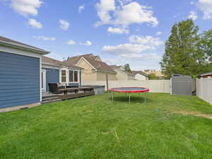 View of yard with a wooden deck, a storage shed, and a trampoline