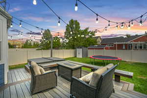 Deck at dusk with a trampoline, a lawn, an outdoor living space with a fire pit, and a storage shed