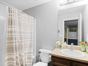 Full bathroom with vanity, toilet, a textured ceiling, and shower / bathtub combination with curtain