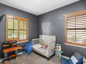 Carpeted bedroom with multiple windows and a nursery area