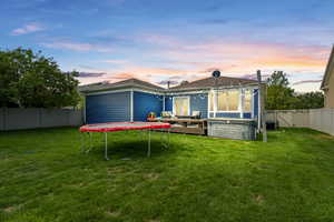 Back house at dusk with a trampoline, a wooden deck, a yard, and a hot tub