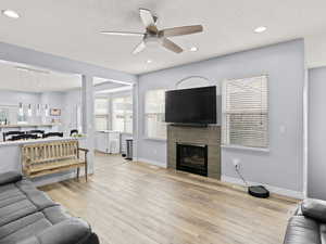 Living room with a fireplace, light wood-type flooring, and ceiling fan