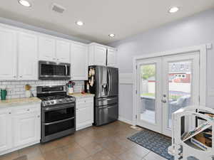 Kitchen with dark tile patterned floors, appliances with stainless steel finishes, white cabinets, french doors, and backsplash