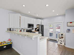 Kitchen featuring decorative backsplash, white cabinetry, appliances with stainless steel finishes, and kitchen peninsula