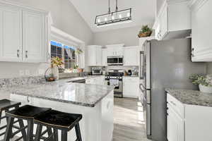 Kitchen featuring kitchen peninsula, appliances with stainless steel finishes, decorative light fixtures, white cabinets, and a kitchen bar