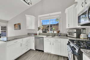 Kitchen featuring light stone countertops, white cabinets, appliances with stainless steel finishes, kitchen peninsula, and vaulted ceiling