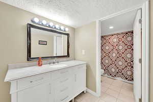 Bathroom with a textured ceiling, tile patterned floors, vanity, and toilet