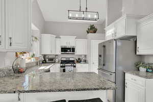 Kitchen with appliances with stainless steel finishes, decorative light fixtures, white cabinetry, sink, and kitchen peninsula