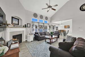 Living room featuring a tile fireplace, light wood-type flooring, high vaulted ceiling, and ceiling fan