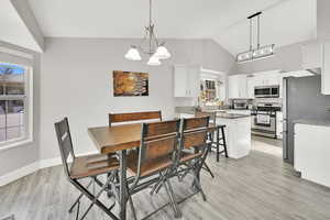 Dining space featuring an inviting chandelier, light hardwood / wood-style flooring, a wealth of natural light, and lofted ceiling