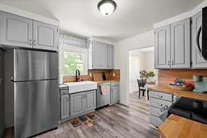 Kitchen featuring tasteful backsplash, gray cabinets, sink, light hardwood / wood-style flooring, and appliances with stainless steel finishes