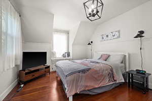 Bedroom featuring vaulted ceiling, dark hardwood / wood-style floors, and a chandelier