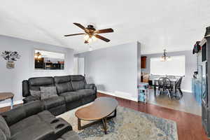 Living room with ceiling fan with notable chandelier, dark wood-type flooring, and a textured ceiling