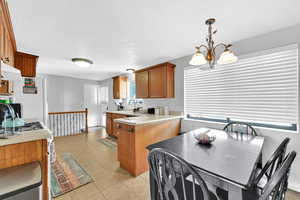 Kitchen with hanging light fixtures, sink, white refrigerator, light tile patterned flooring, and an inviting chandelier