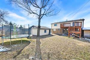 Back of property featuring a trampoline, an outdoor structure, and a wooden deck