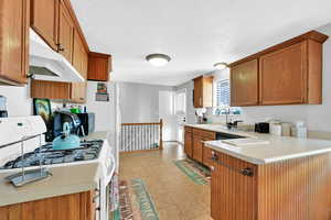 Kitchen featuring sink, a textured ceiling, white range with gas cooktop, and light tile patterned flooring