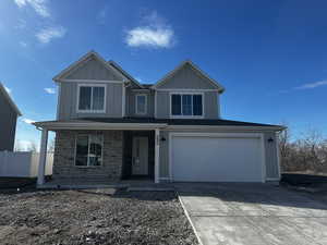 View of front of property featuring stone siding, fence, concrete driveway, board and batten siding, and covered porch