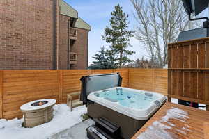 Snow covered patio featuring an outdoor fire pit, a hot tub, and a wooden deck