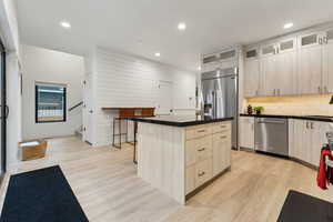 Kitchen with stainless steel appliances, light brown cabinetry, light hardwood / wood-style floors, and a center island