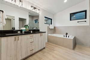 Bathroom featuring a relaxing tiled tub, hardwood / wood-style floors, and vanity