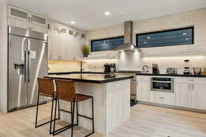 Kitchen featuring wall chimney range hood, a center island, sink, appliances with stainless steel finishes, and a breakfast bar area