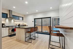 Kitchen with ventilation hood, stainless steel stove, light hardwood / wood-style floors, and a center island