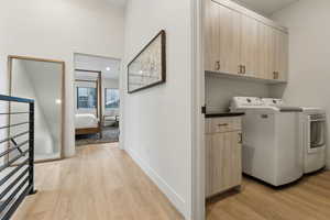 Laundry room featuring washer and clothes dryer, light wood-type flooring, and cabinets