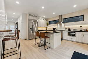 Kitchen featuring backsplash, wall chimney range hood, light hardwood / wood-style floors, a kitchen island, and stainless steel appliances