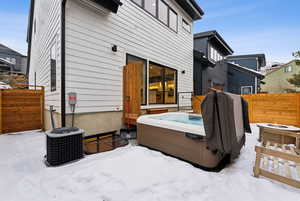 Snow covered back of property with an outdoor fire pit, cooling unit, and a hot tub