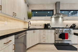 Kitchen with backsplash, range hood, light hardwood / wood-style floors, sink, and appliances with stainless steel finishes