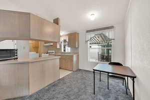 Kitchen with sink, washer and clothes dryer, white range with gas stovetop, light brown cabinets, and a textured ceiling