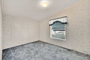 Unfurnished room featuring lofted ceiling, a textured ceiling, and dark colored carpet