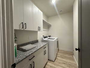 Laundry area featuring cabinets, a textured ceiling, light wood-type flooring, and washing machine and clothes dryer