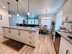 Kitchen with light stone countertops, white cabinetry, hanging light fixtures, light wood-type flooring, and stainless steel dishwasher